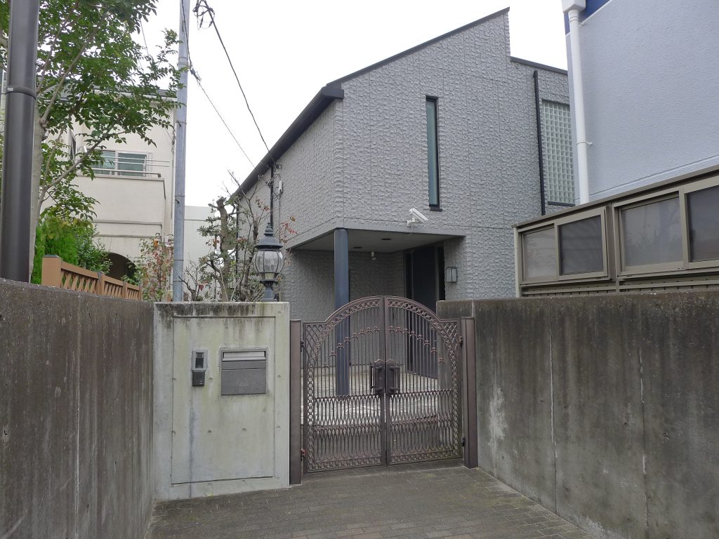 塀に挟まれた細い通路の先に建つ住宅